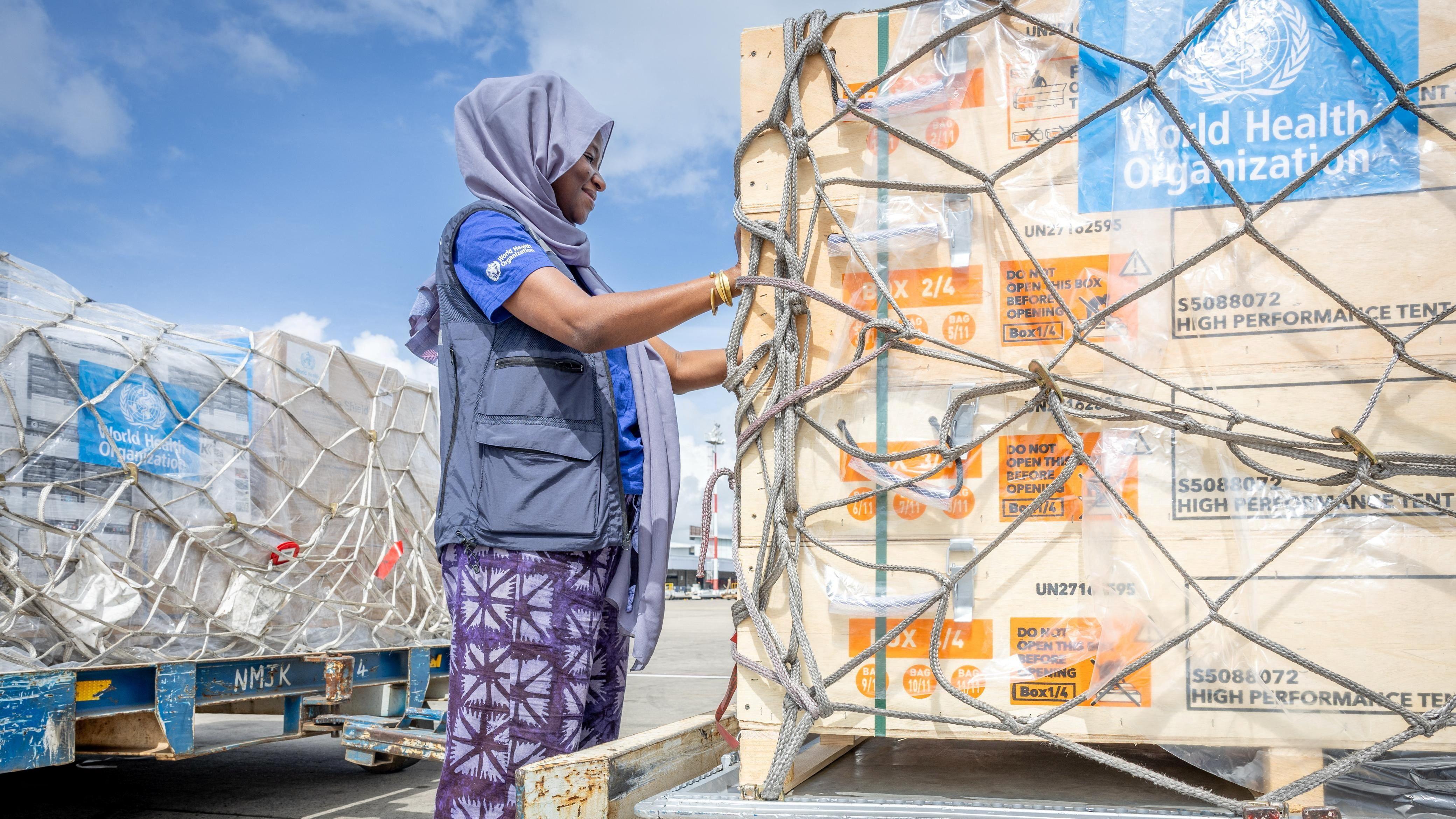 Mulher inspeciona grandes caixas de ajuda humanit&aacute;ria em pallets de transporte