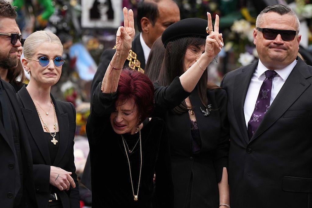 Sharon Osbourne con los dedos de las manos en símbolo de paz hacia los fanáticos presentes en el funeral