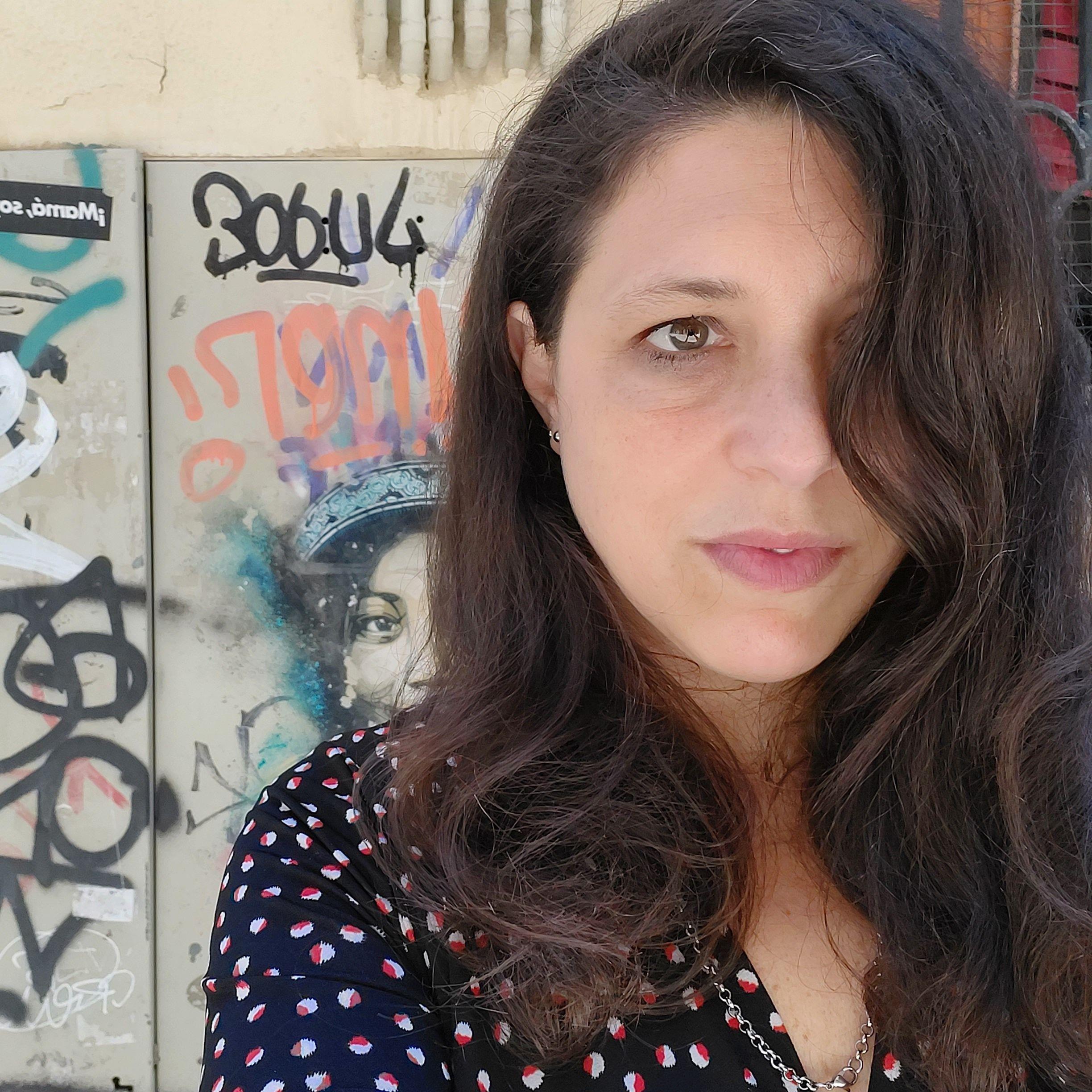 Una selfi de Ariana Harwicz con un mechón de pelo que le cubre el ojo izquierdo. En el fondo, se ven algunos grafitis.