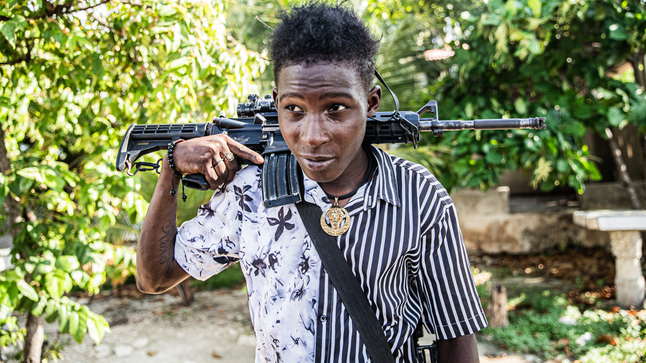 Um jovem membro de gangue de 14 anos com um fuzil AK-47 nos ombros e um medalh&atilde;o dourado no pesco&ccedil;o patrulha as ruas do bairro Mariani, de Porto Pr&iacute;ncipe (Haiti), em 6 de outubro de 2025, perto da Route Nationale 2, parcialmente tomada pelas gangues