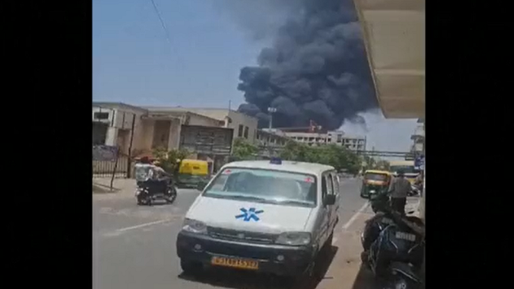 Un vehículo blanco estacionado en una calle y en el fondo se ve una nube de humo negro