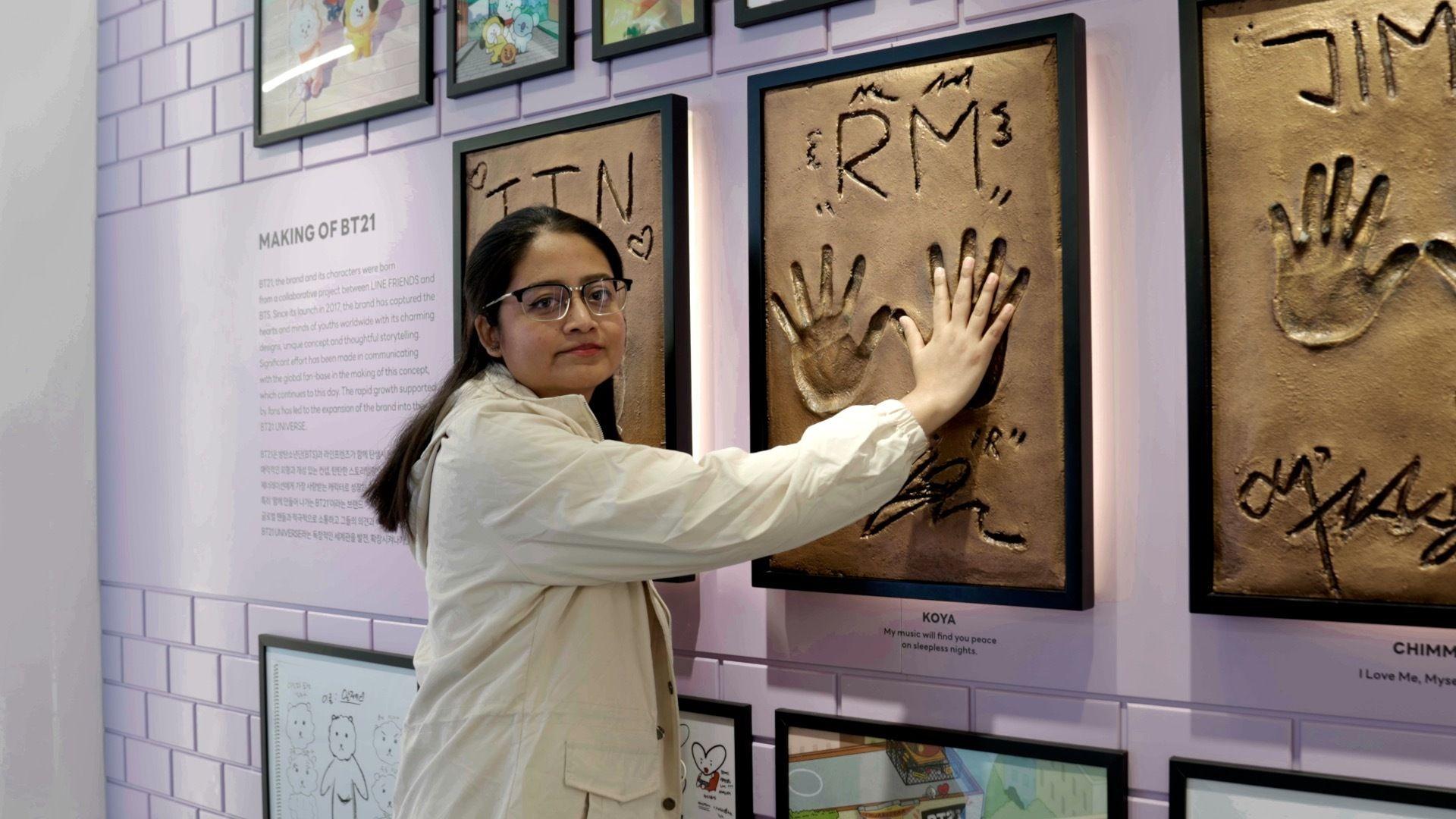 한 여성이 BTS 멤버 RM의 손을 본뜬 액자에 자신의 손을 갖다대고 있따 