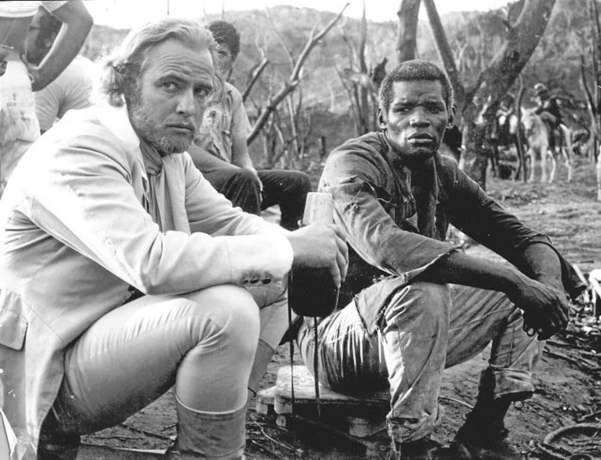 Foto en blanco y negro de Marlon Brando y Evaristo Márquez durante la filmación de "Queimada". Ambos están sentados durante un descanso. 