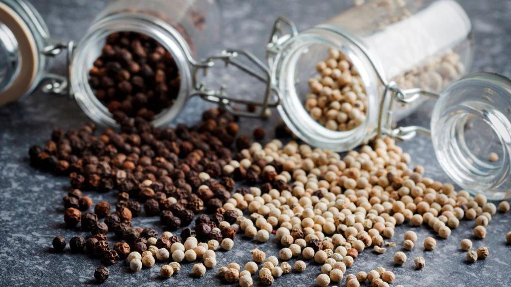 Dos botes derramados de pimienta negra y pimienta blanca