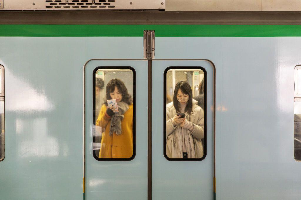 امرأتان تظهران من زجاج عربة المترو وتنظران إلى الهاتف الذكي