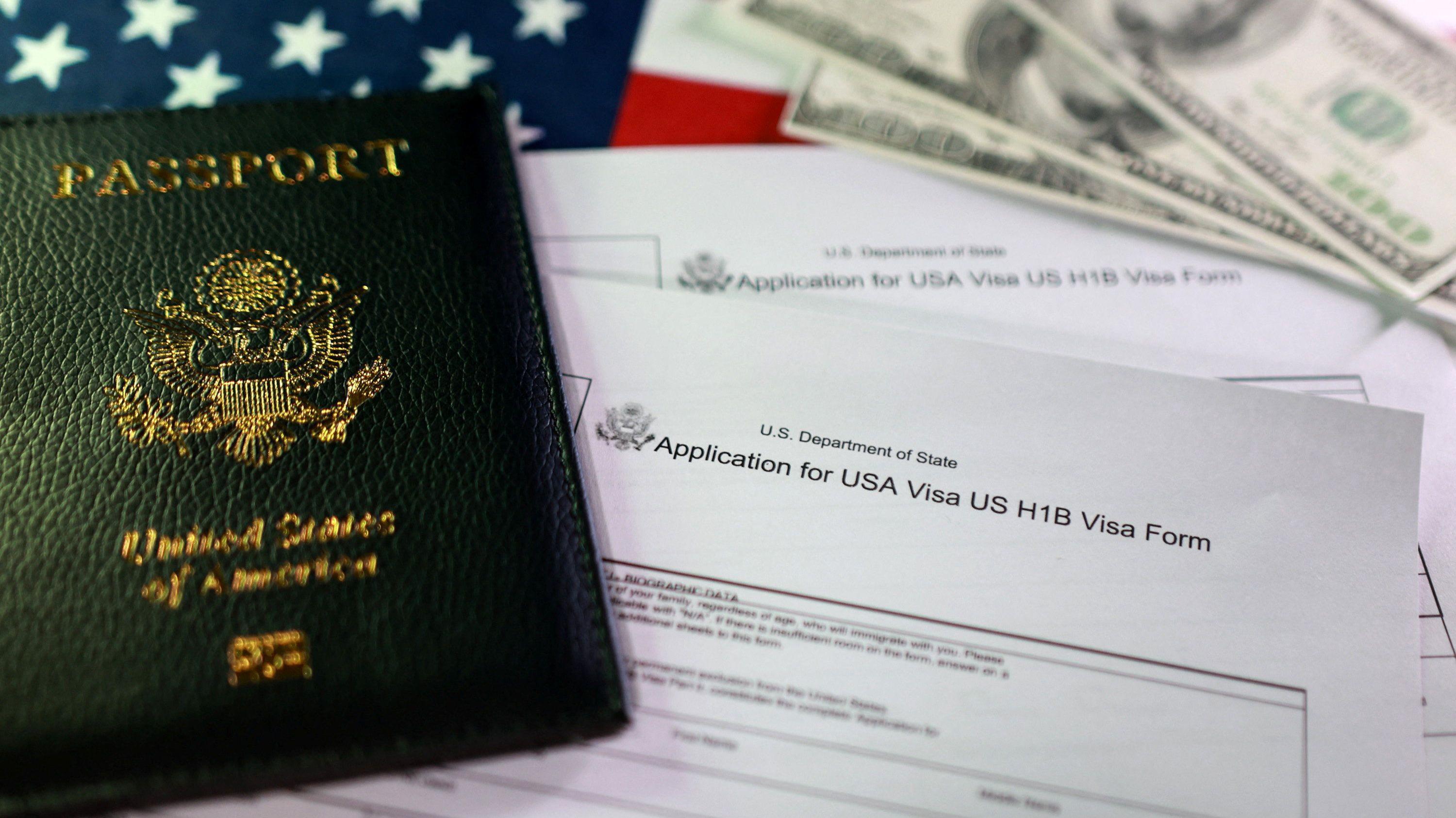 Una composicón de un pasaporte con las palabras borrosas sobre una solicitud para la visa H-1B con la bandera de EE.UU. de fondo y dólares.