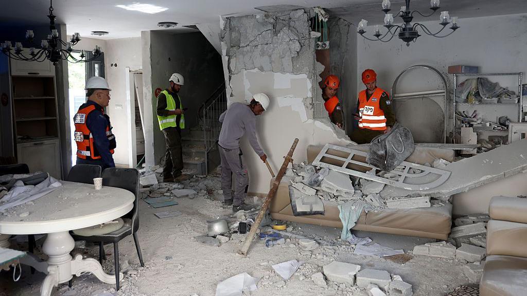 رجل إطفاء يرتدون الخوذ وثياب العمل في منزل متضرر جدرانه محطمة جراء سقوط صاروخ قرب تل أبيب