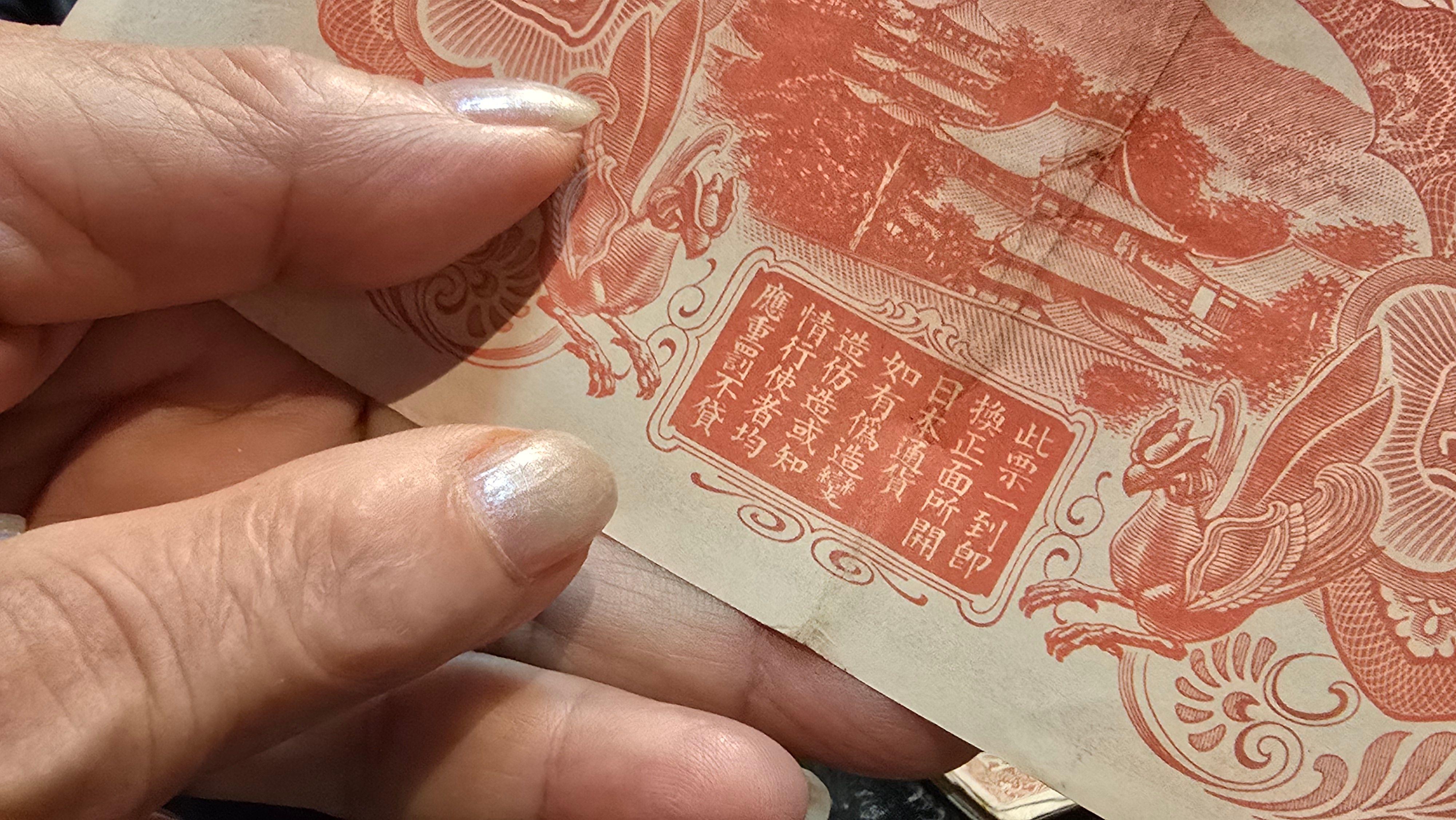 一位香港索償協會會員指著一張紅色100圓日本軍票背面所印字樣：「此票一到即換正面所開日本通貨」（BBC中文圖片）