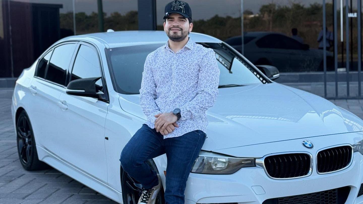 César Gastélum sentado sobre un BMW blanco. Lleva una gorra negra