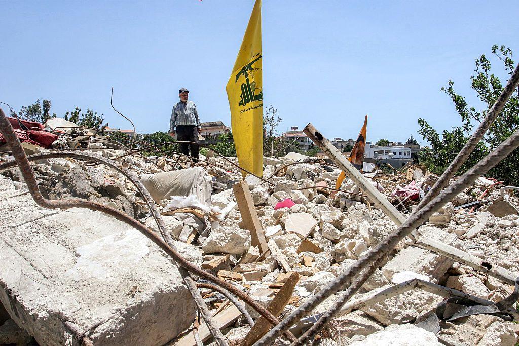 Una bandera amarilla de Hezbolá se erige de los escombros de lo que pudo ser un edificio.