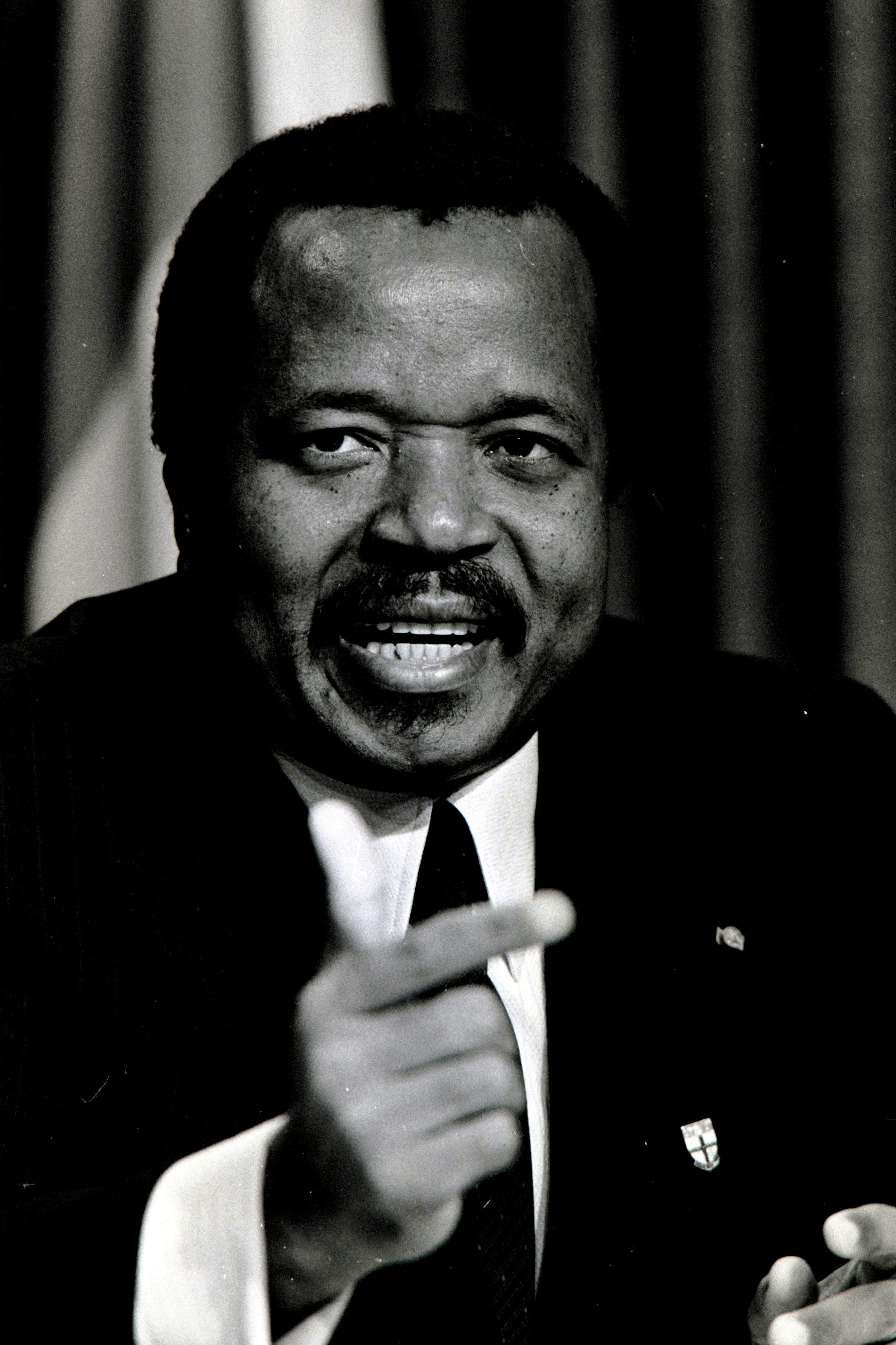 Fotografía en blanco y negro del presidente de Camerún, Paul Biya, de aspecto más joven, con traje y haciendo un gesto con la mano derecha.