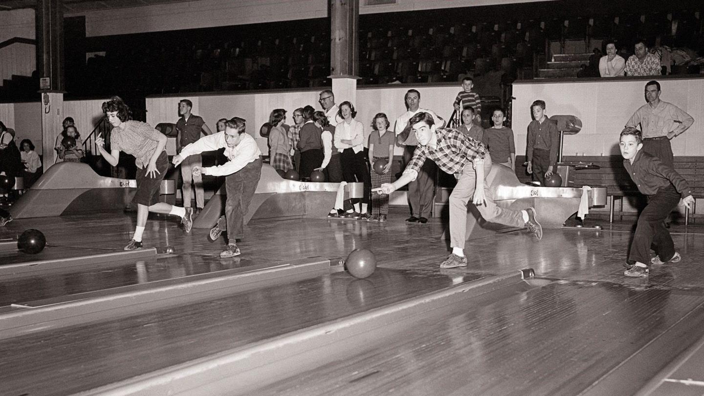 一張黑白照片，照片中是正在打保齡球的年輕男女。