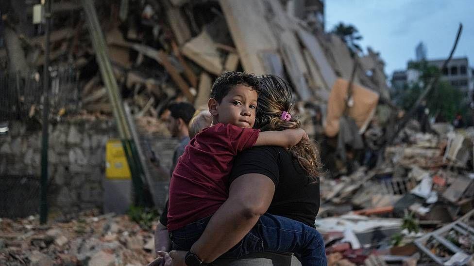 Un niño en Caracas, en brazos de su madre, mira a la cámara. Detrás se ven los escombros de edificios destruidos por los terremotos