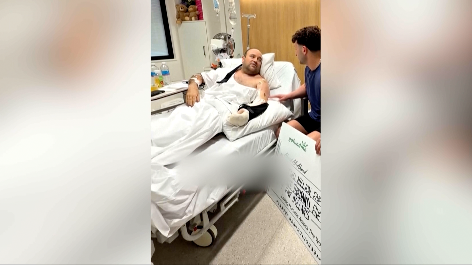 Ahmed al Ahmed, recostado en una cama de hospital con el brazo derecho vendado, recibe un cheque gigante donde se puede ver escrita la suma de 2 millones quinientos mil