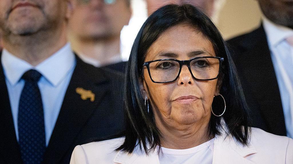 Delcy Rodríguez, vistiendo un traje blanco y gafas de montura negra.