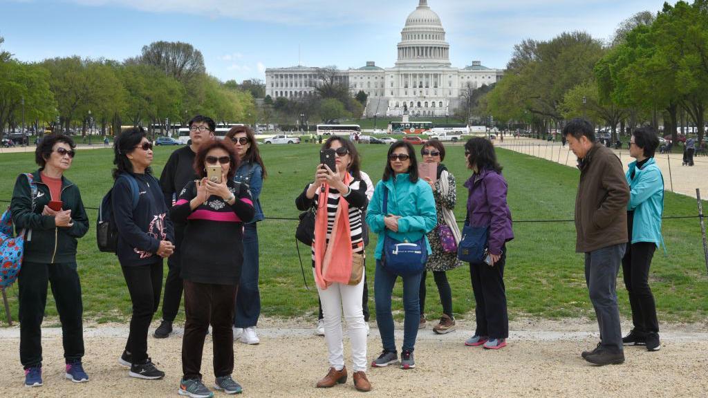 Um grupo de turistas chineses tira fotos com o Capitólio dos EUA ao fundo. 