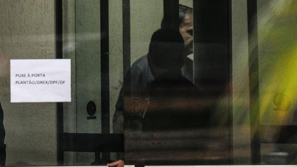 Jair Bolsonaro por trás da porta de vidro da Superintendência da Polícia Federal de Brasília neste domingo.