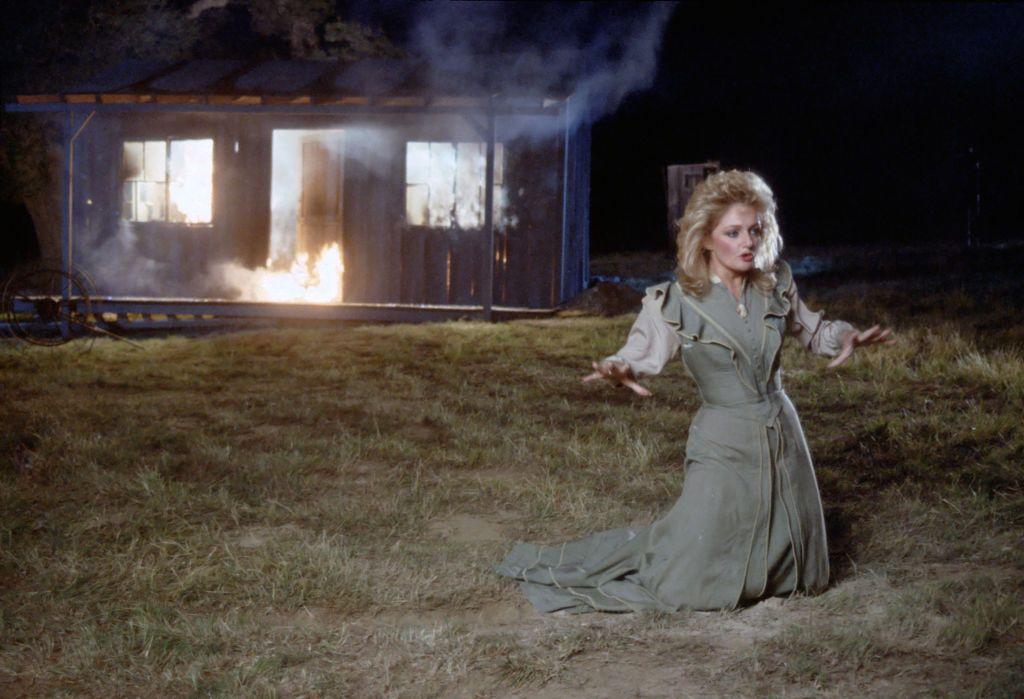 Bonnie Tyler con un vestido antiguo, cantando en frente de una casa de madera que se quema.