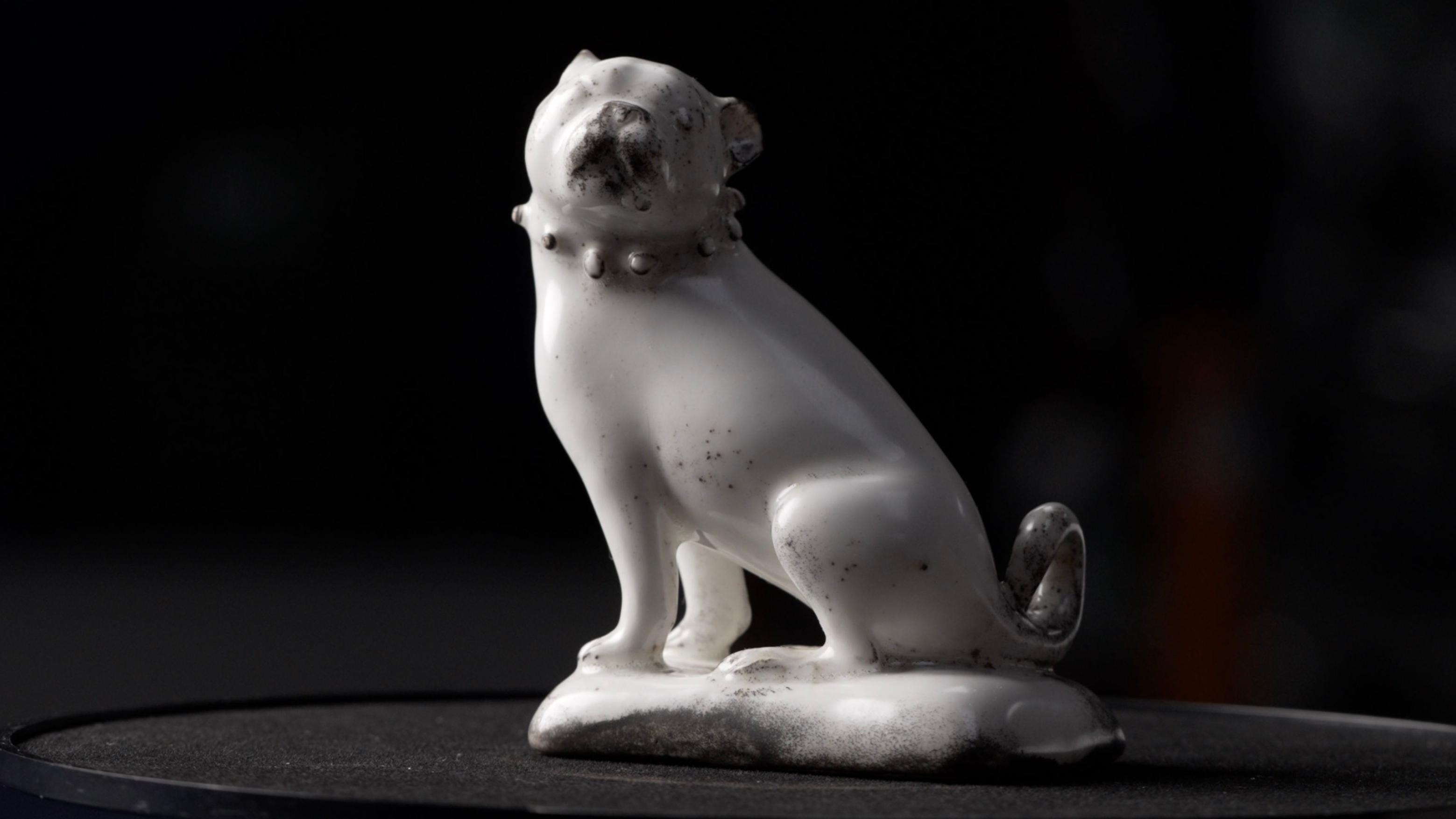 Uma estatueta inteira de um pug sentado, feita de porcelana branca esmaltada, com detalhes em preto, encontrada em St James&rsquo; Gardens, em Euston