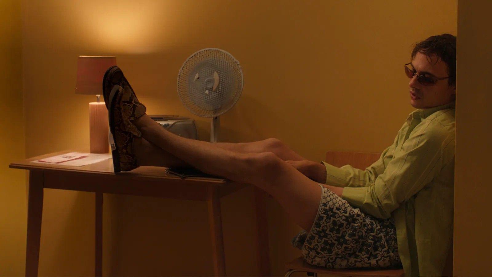 Homem sentado em cadeira com os pés apoiados em cima de uma mesa