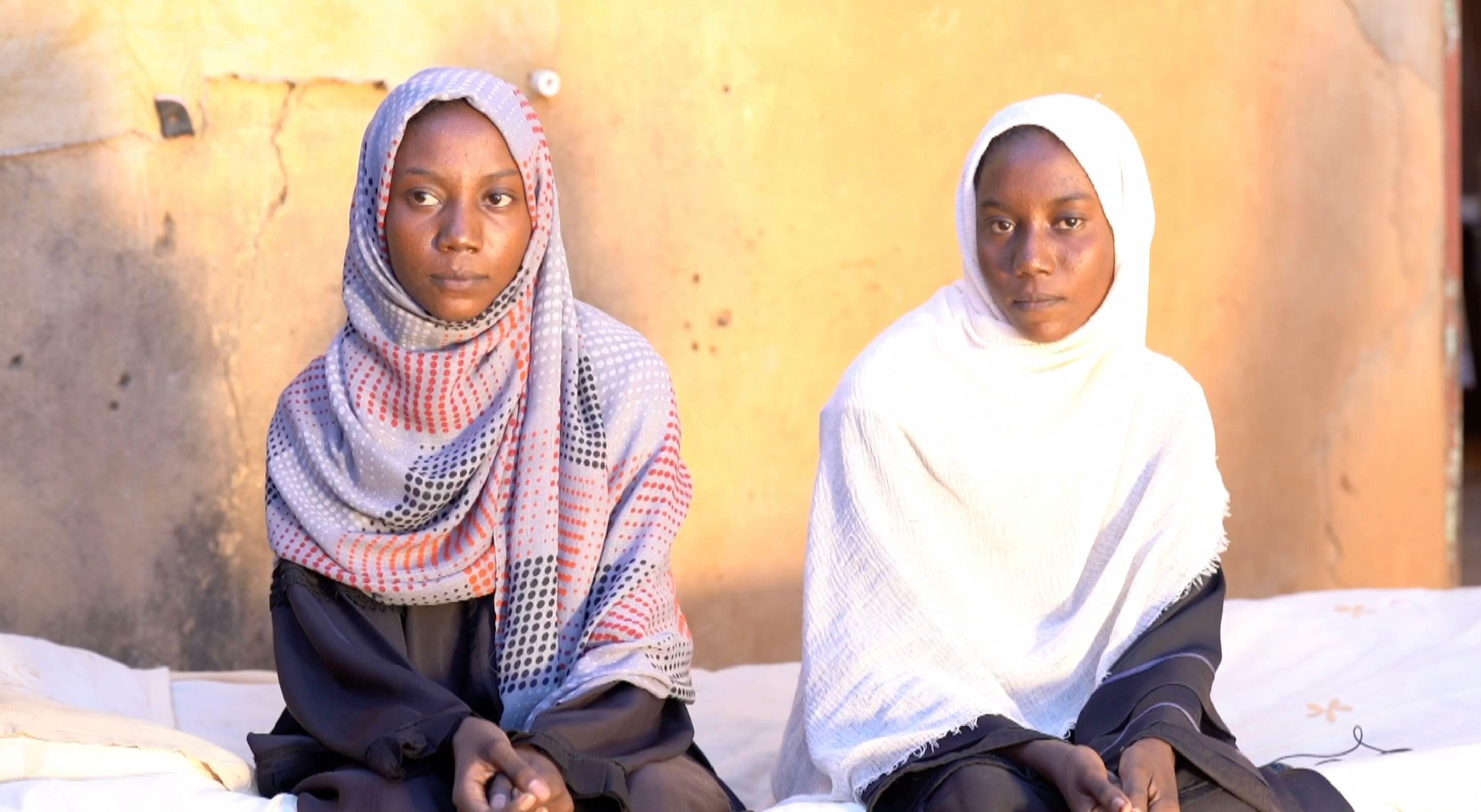 فتاتان سودانيتان ترتديان غطاء رأس (حجاباً) تجلسان بجوار بعضهما.