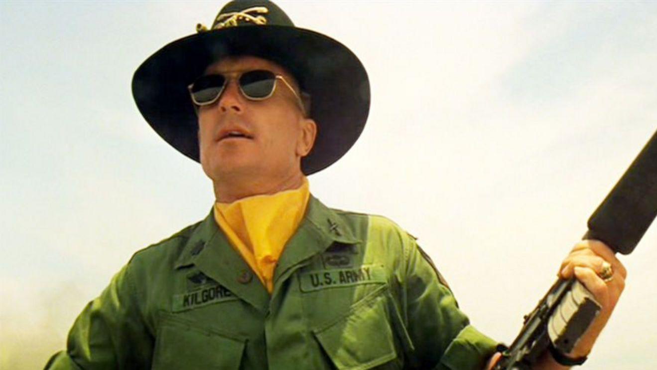 روبرت دوفال في مشهد من "القيامة الآن" بزي عسكري كتب عليه يو أس أرمي - الجيش الأمريكي - مع قبعة عسكرية وبندقية في يديه اليمنى