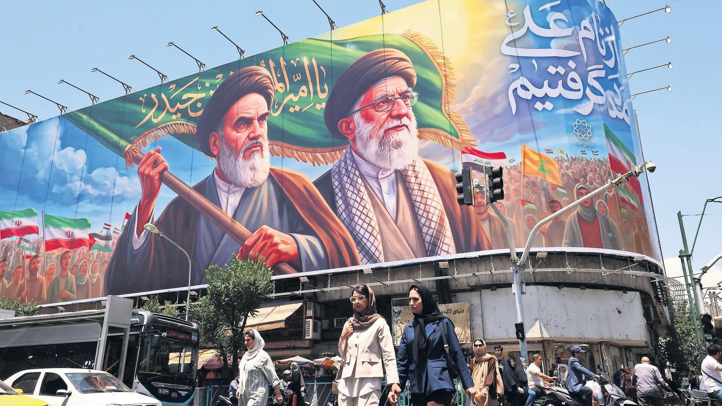 إيرانيون يسيرون في أحد شوارع طهران وخلفهم لوحة جدارية ضخمة للمرشدين الراحلين الخميني وخامنئي