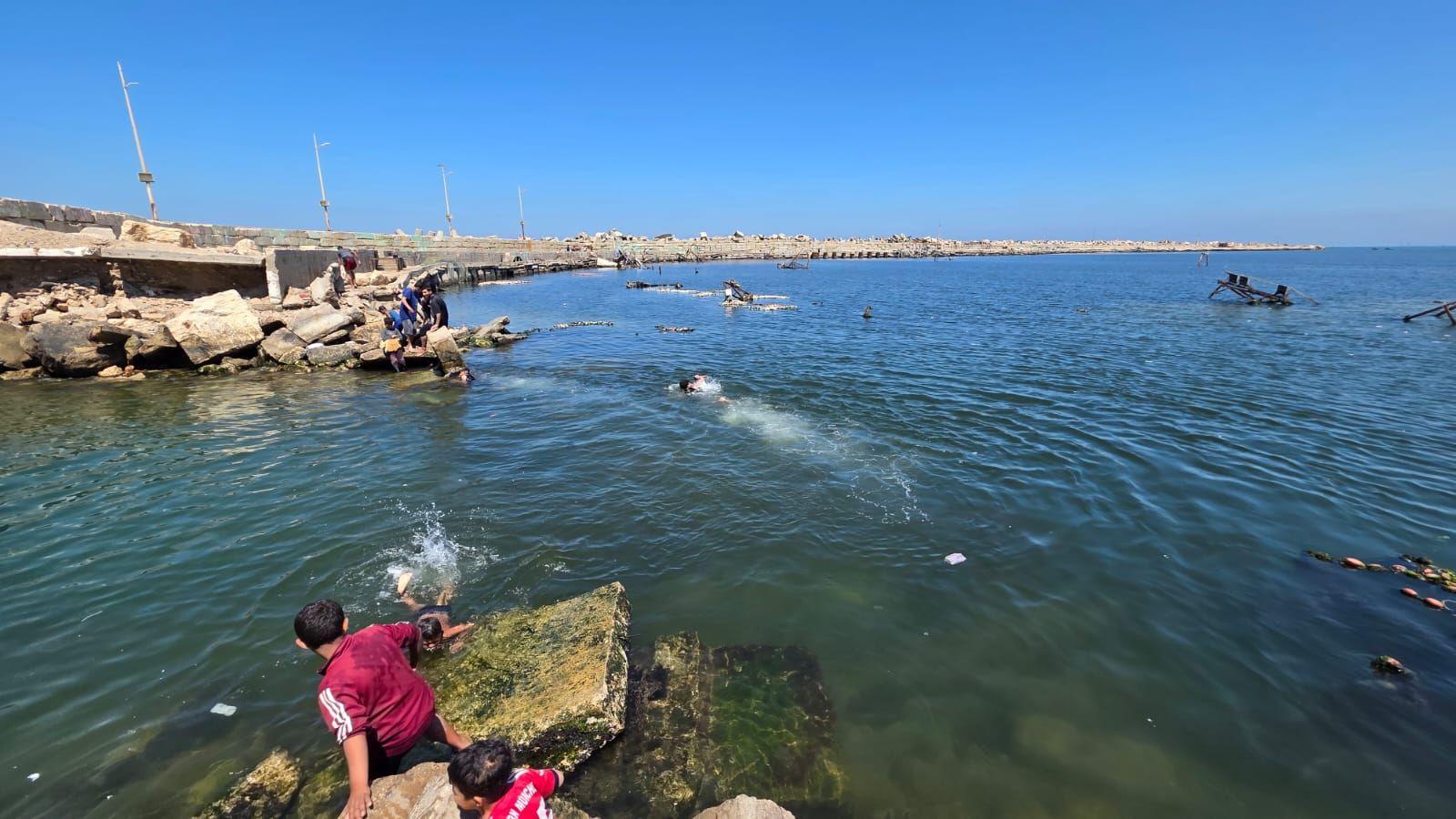أشخاص بينهم أطفال في البحر مقابل ميناء غزة