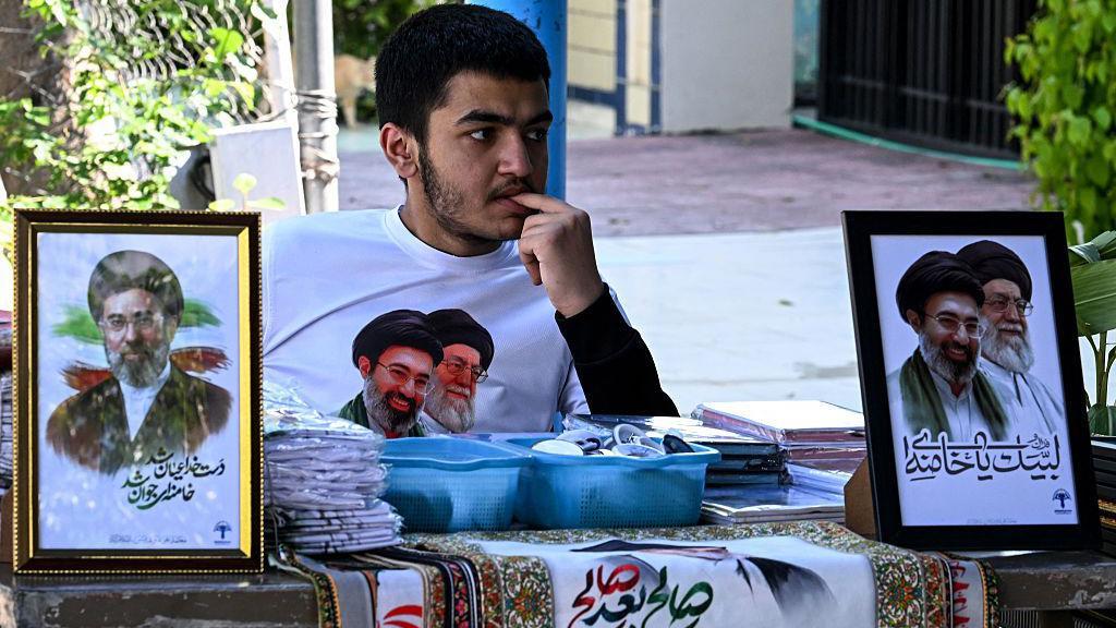 2026年4月5日，在伊斯蘭堡的一座什葉派清真寺外，一名商販正在出售伊朗已故最高領袖阿亞圖拉·阿里·哈梅內伊（Ayatollah Ali Khamenei）及其兒子、現任最高領袖穆傑塔巴·哈梅內伊（Mojtaba Khamenei）的相框，等待顧客光臨。