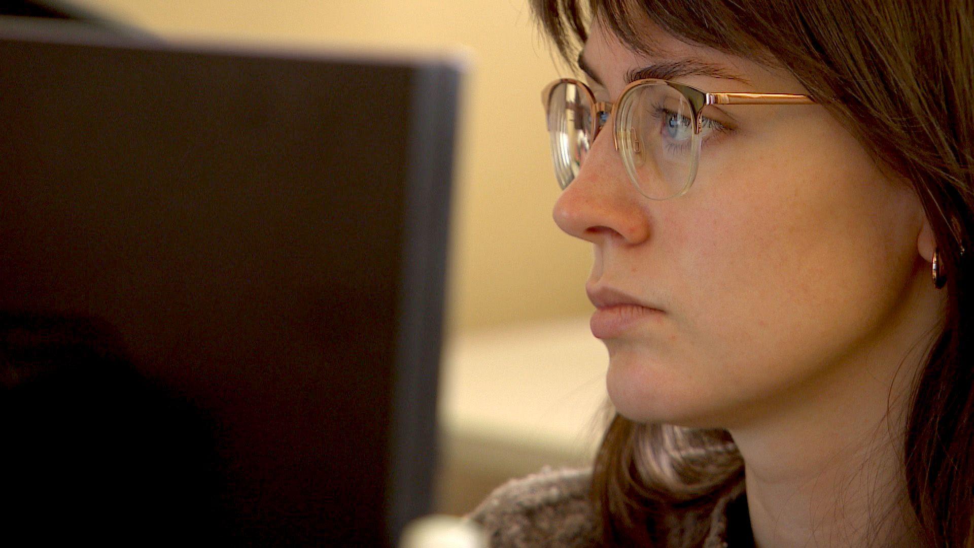 Una mujer joven con gafas mira la pantalla de una computadora