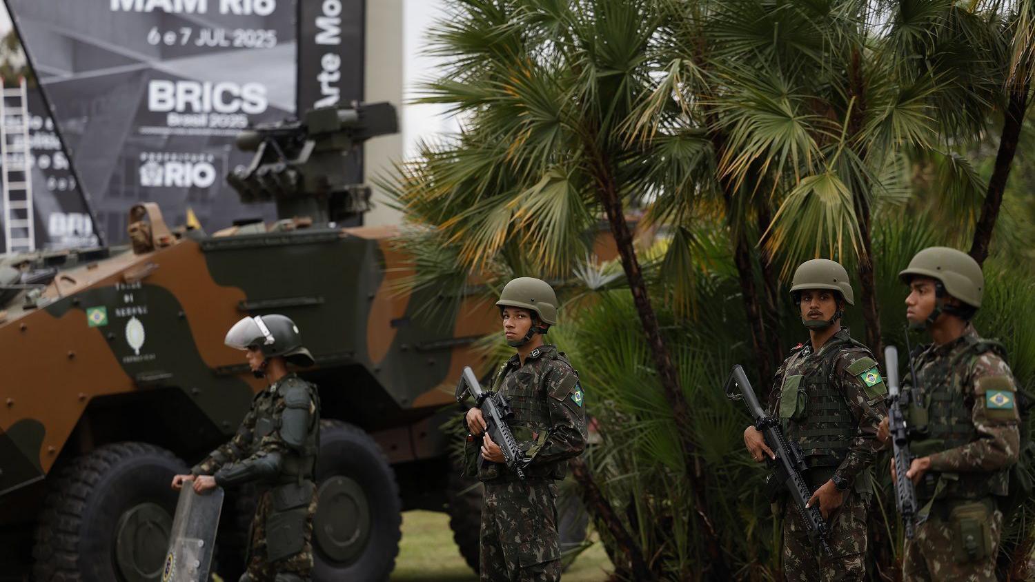 Foto com militares enfileirados segurando armas ao lado de um tanque. No fundo, é possível ler Brics em uma placa, indicando o evento. 