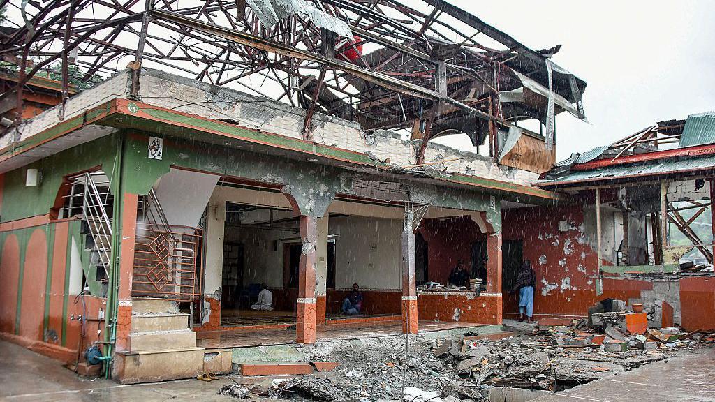 A heavily damaged mosque, its roof almost entirely torn away and its steel framework twisted and exposed against a grey sky.