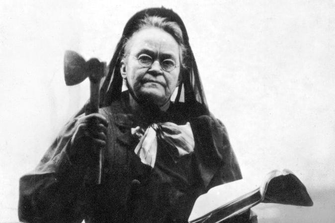 Carrie Nation sostiene un hacha en una mano y la Biblia en otra