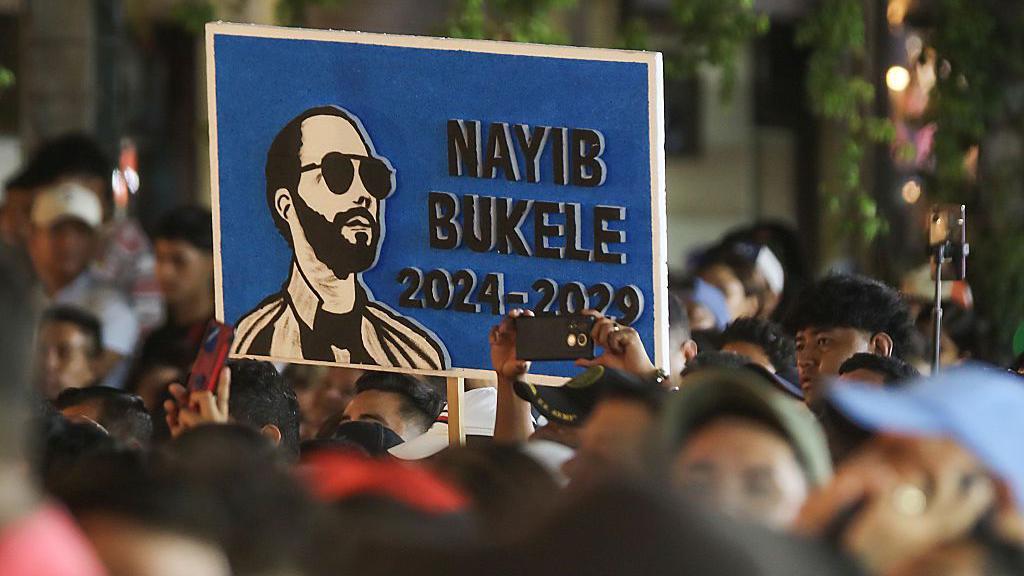 Salvadoreños reunidos afuera del Teatro Nacional en el centro histórico de San Salvador, El Salvador, para escuchar el mensaje del presidente Nayib Bukele con motivo de sus seis años al frente del gobierno sostienen un cartel en su apoyo, el 1 de junio de 2025. (Foto de Alex Peña/Getty Images)