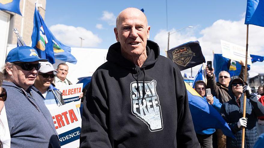 Mitch Sylvestre, director de Stay Free Alberta, un hombre de mediana edad, con poco pelo, viste una sudadera negra que lee "Queda libre" sobre el mapa de la provincia de Alberta.
