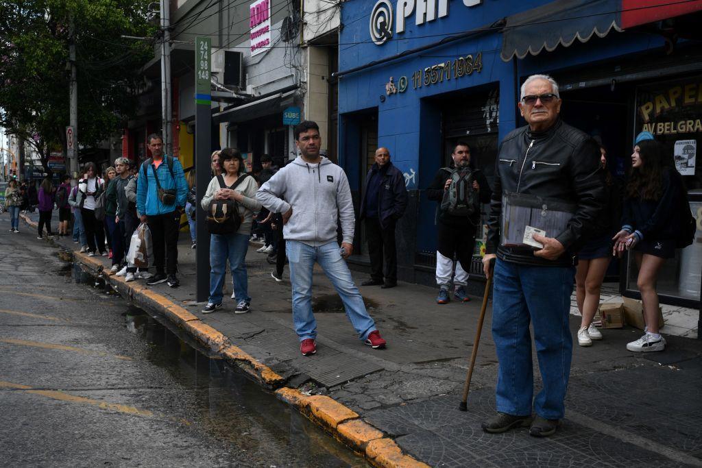 Un grupo de personas espera un autobús parados en una acera de una avenida en Buenos Aires