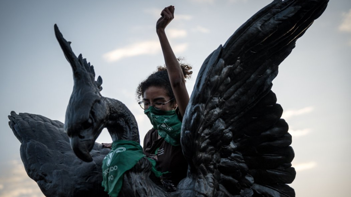 Uma jovem com lenço verde se manifestando em uma estátua