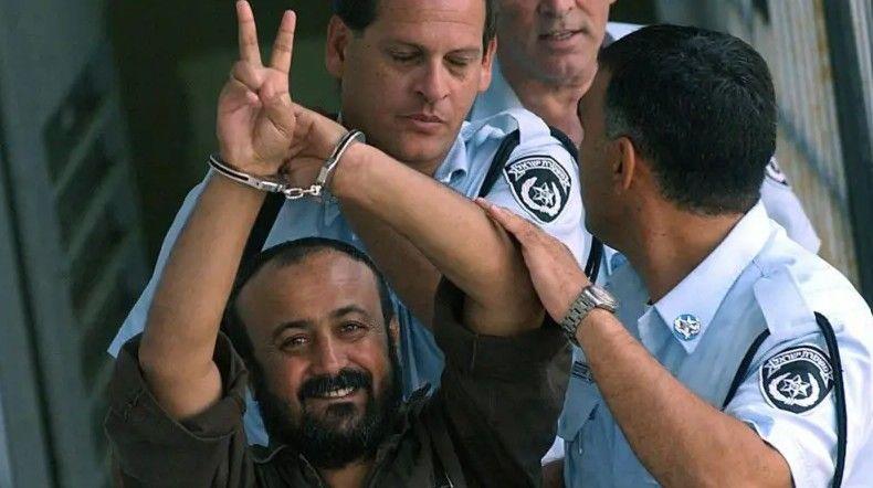 صورة أرشيفية لمروان البرغوثي مقيداً بالأصفاد وخلفه شرطة إسرائيلية، ويرفع علامة النصر.
