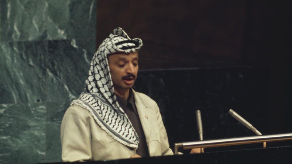 العضوية المؤجّلة: ما الذي يقف بين الفلسطينيين ومقعد الأمم المتحدة؟ 1 ياسر عرفات، مرتدياً الكوفية الفلسطينية وبزة عسكرية، يلقي خطاباً أمام الجمعية العامة للأمم المتحدة في نيويورك عام 1974