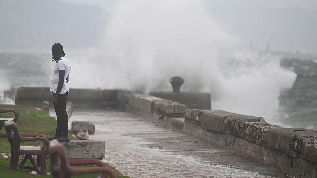 Un hombre mira las olas provocadas por la tormenta Melissa en Kingston