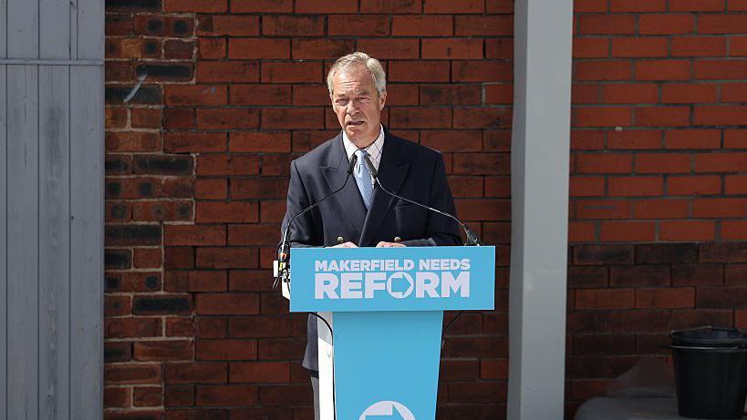 El líder de Reform UK, Nigel Farage, habla en una conferencia de prensa sobre un atriz azul claro.