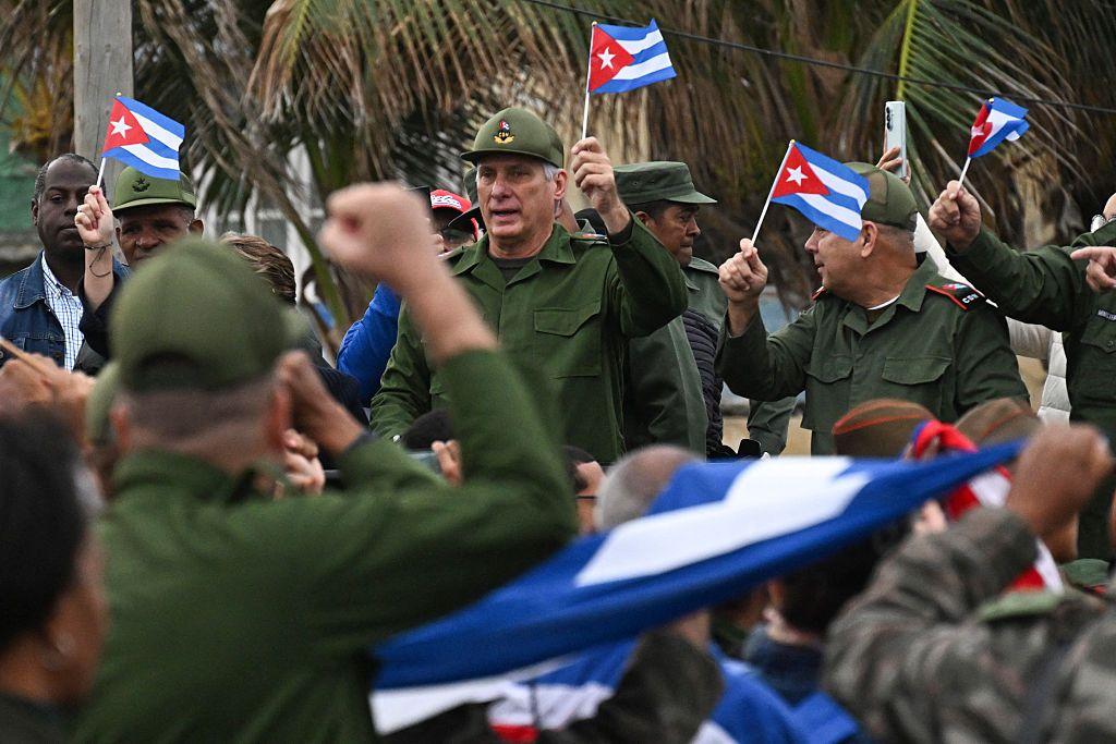 Miguel Díaz-Canel, sosteniendo una bandera cubana vestido con uniforme militar, junto a otros oficiales del ejército