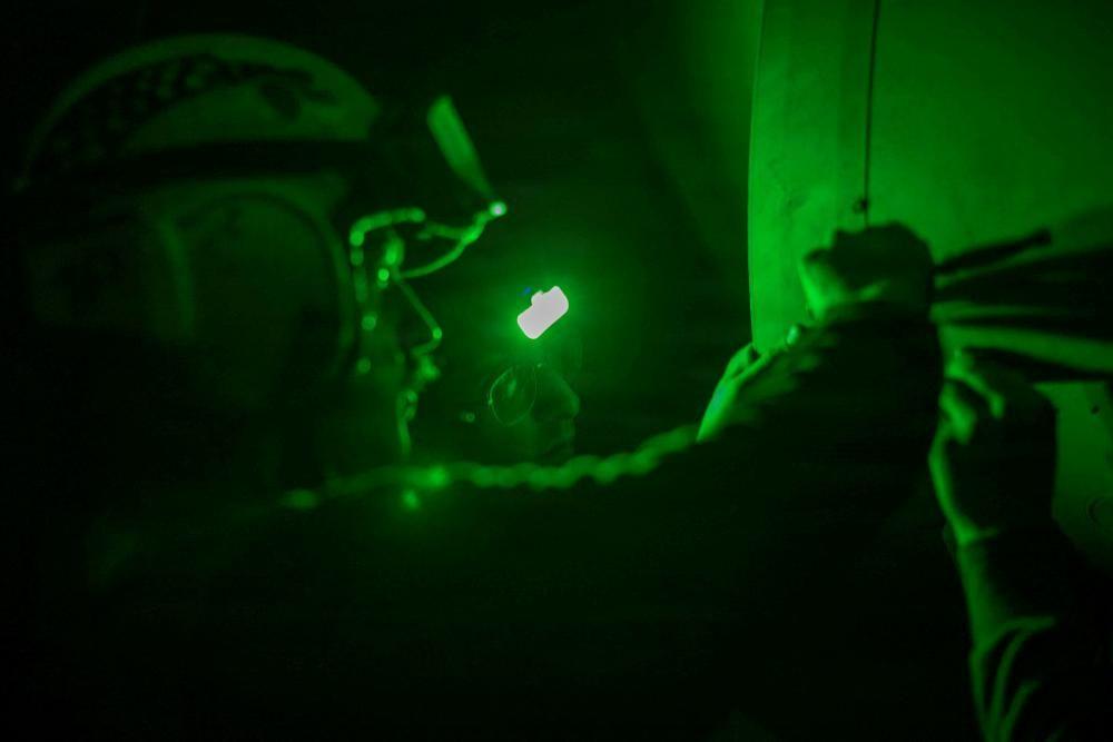 Dos tripulantes del USS Abraham Lincoln trabajando con una lámpara de luz verde en la noche