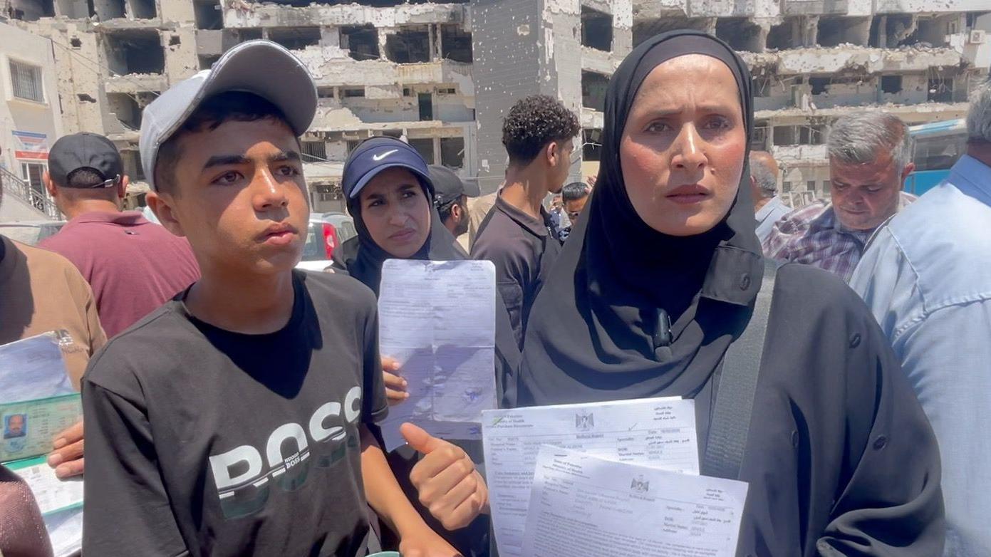 أم سمير الديني (يمين) تقف بجانب ابنها معاذ، الذي يستخدم عكازين (يسار)، خارج مستشفى الشفاء في مدينة غزة، شمال غزة