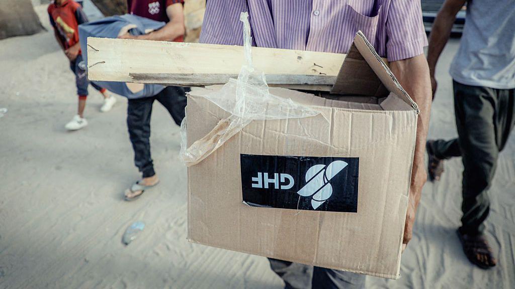 صورة تظهر نازحاً فلسطينياً في قطاع غزة يحمل صندوق مساعدات يحمل شعار "مؤسسة غزة الإنسانية".