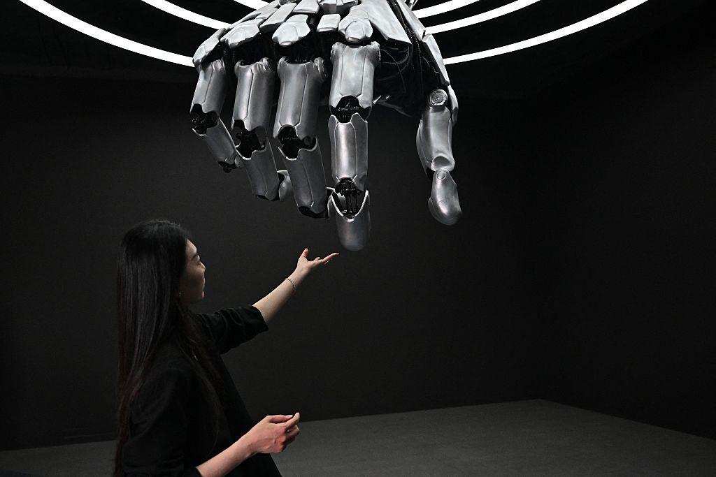 Una mujer toca una mano robótica durante una gira de prensa por el centro de exposiciones Robot World en Pekín el 17 de abril de 2025.