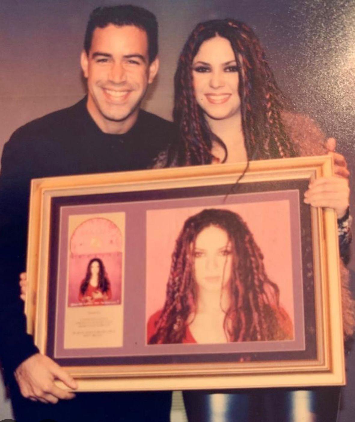 O executivo Luiz Calainho e a cantora Shakira sorriem para a c&acirc;mera enquanto seguram um quadro emoldurado com a imagem promocional de um &aacute;lbum da cantora.