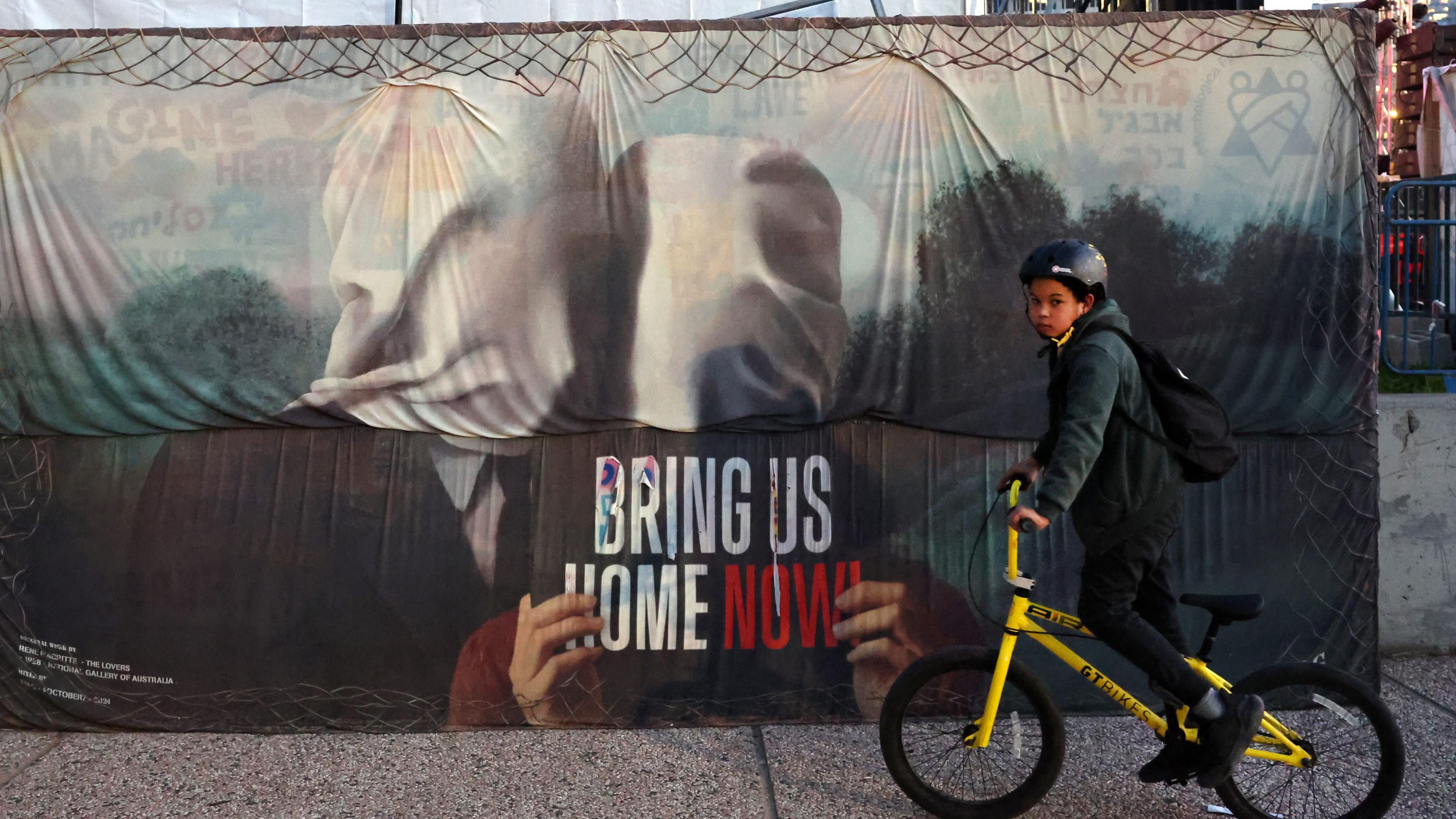 Kako odrastanje u ratu zaista utiče na jednog 11-godišnjaka 15 Dečak vozi bicikl pored postera u kojem se zove na oslobađanje talaca