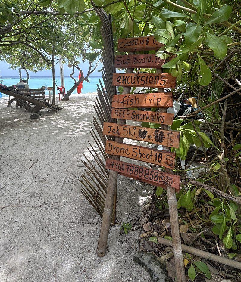 Placas oferecendo opções de atividades em um resort nas ilhas Maldivas, com uma pessoa e o mar ao fundo