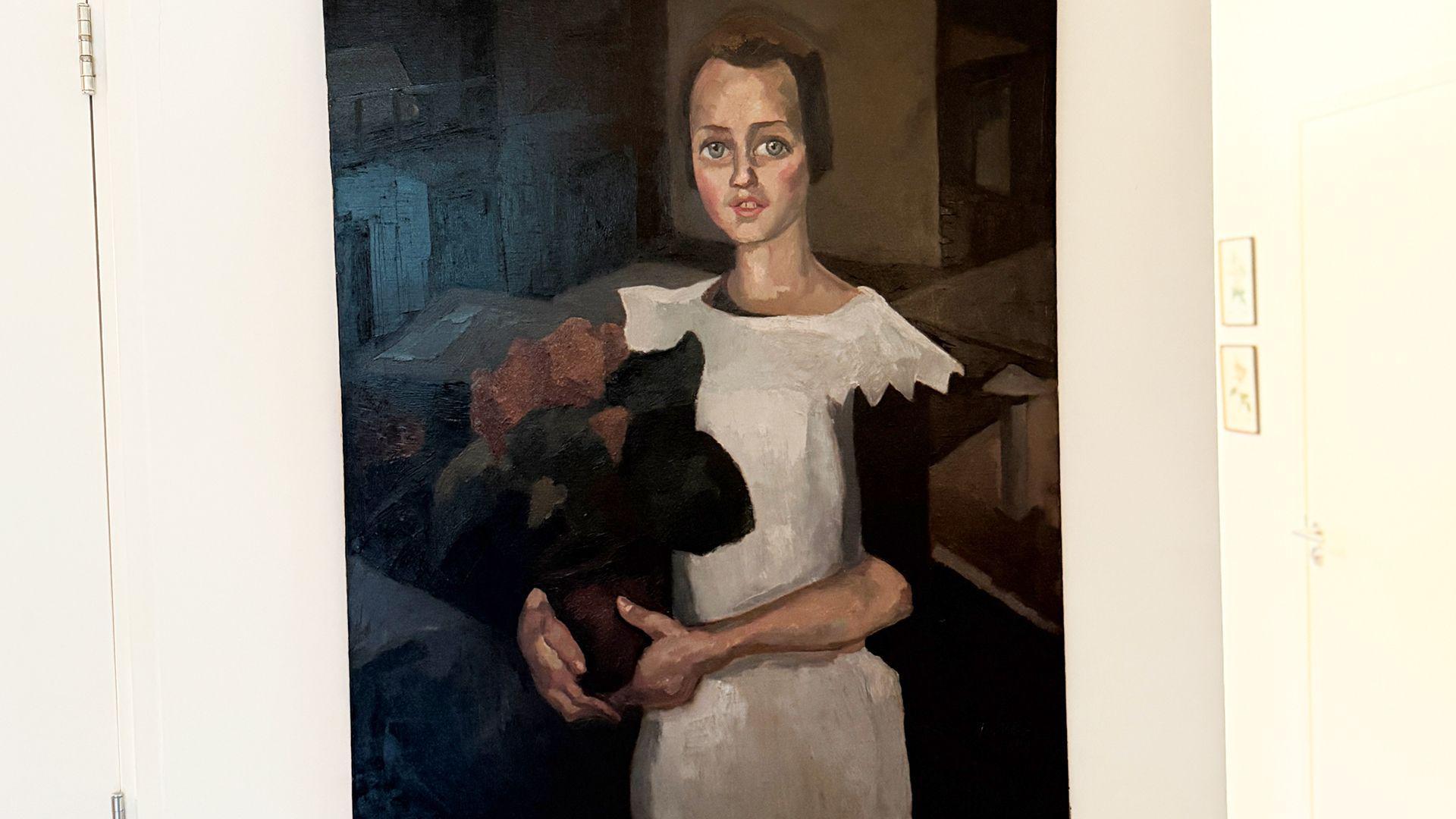 Un cuadro que se cree que es el "Retrato de una joven" de Toon Kelder muestra a una niña con un vestido blanco de mangas negras que sostiene lo que parece ser un ramo de flores rojas. Tiene el pelo castaño y los ojos azules, y está sentada.
